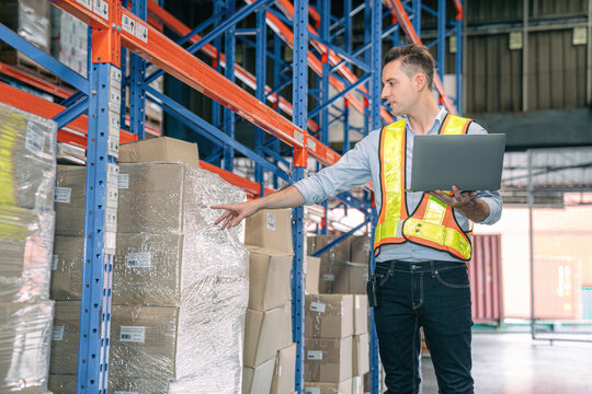 Smart smiling caucasian warehouse man,worker,manager use laptop to check goods on shelf for product distribution stock management, Logistics shipping business planning concept with copy space