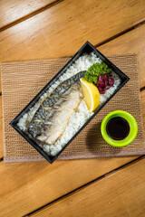 A bento box of white rice topped with grilled mackerel fillet served with lemon wedge and pickled vegetables.