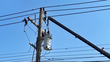 Electricity maintenance worker repairing power line pole equipment with crane lifting transformer ensuring safety and reliable power supply under clear blue sky conditions