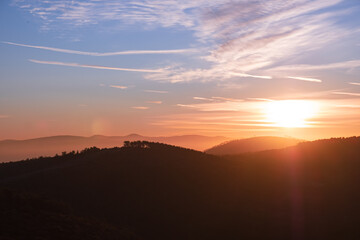 Breathtaking landscape view of silhouetted mountain ridges and hills under a dramatic colorful sky at sunrise