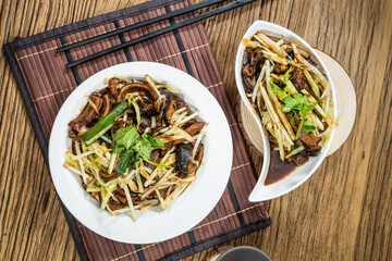 Two plates of stir fried eel slices mixed with bean sprouts and green herbs served on bamboo mats.