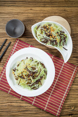Two plates of shredded black fungus mixed with cucumber strips and garlic served on bamboo mats.