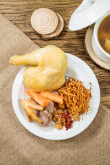 A plate of boiled chicken served with roots, berries, and herbs beside a ceramic soup pot.