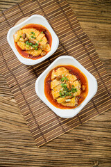 Two plates of tofu cubes served in spicy chili oil garnished with sesame seeds and green herbs.