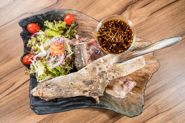 A decorative plate with grilled fish served alongside fresh salad and a glass of soy-based dipping sauce.