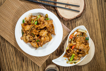 A plate of stir-fried pork slices cooked with green onions and vegetables in savory sauce, served on white ceramic dishes on a wooden table.