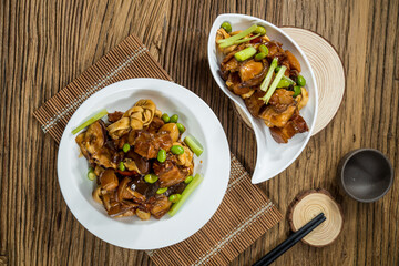 A plate of braised chicken pieces cooked with edamame beans and bamboo shoots in savory sauce, served on white ceramic dishes.