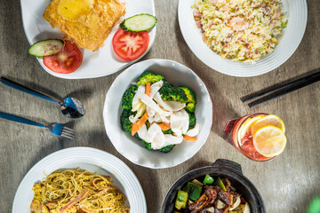 A table with multiple Chinese dishes including fried noodles, stir-fried vegetables, fried rice, and braised beef served in various plates.