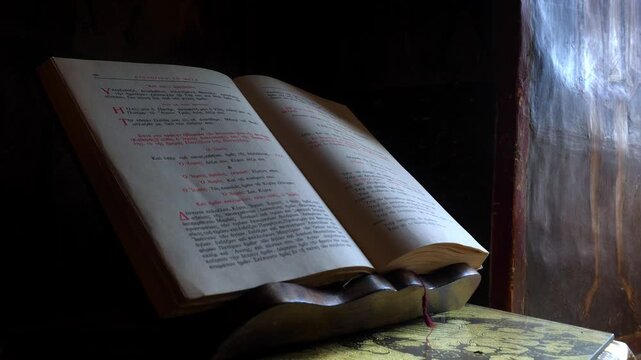 Close-up of an open ancient liturgical book with Greek text resting on a wooden stand inside an Eastern Orthodox monastery in Meteora, Greece