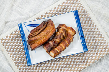 A rectangular ceramic plate with slices of golden-brown pan-fried pork belly arranged neatly for a rich and savory presentation.