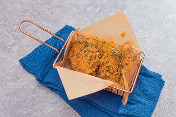 A basket of golden fried chicken pieces coated with herb seasoning, served on parchment paper over a blue cloth for a stylish look.