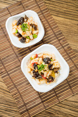 Two plates of cold jellyfish salad mixed with black fungus, vegetables, and light dressing, served on a bamboo mat for a refreshing look.