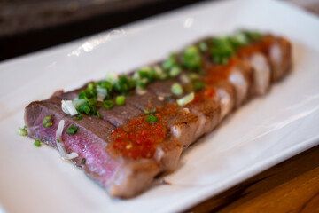 Japanese sliced medium rare steak served on plate, topped with sliced spring onion and sauce