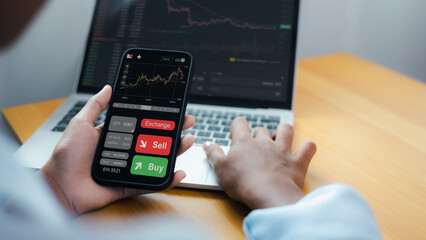 Investor Using Smartphone and Laptop for Cryptocurrency Trading and Stock Market Analysis