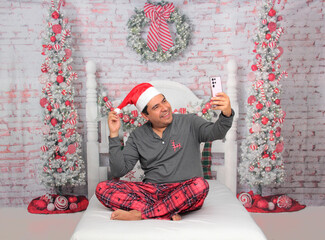Dark-skinned Latino adult man uses his cell phone to make calls, send messages, and shop while celebrating Christmas remotely and alone