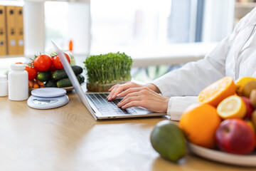 A nutritionist is working on a laptop surrounded by fresh fruits, vegetables, and supplements, emphasizing healthy eating.