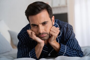 Pensive Man in Pajamas Lying on Bed, Looking at Camera