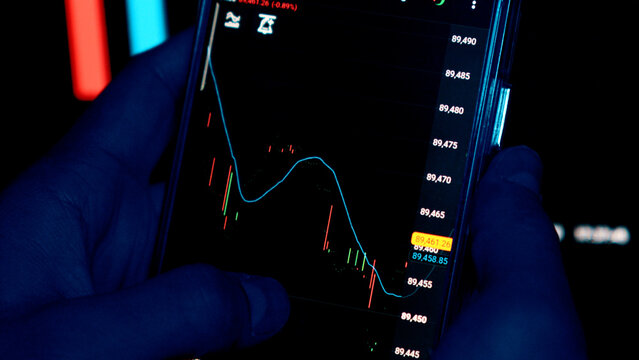 Hands holding a phone with financial growth charts in the dark - Powered by Adobe