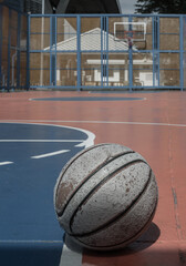 A worn basketball sits on the vibrant orange outdoor court; the hoop and fiberglass backboard are visible in the background. Copy space.
