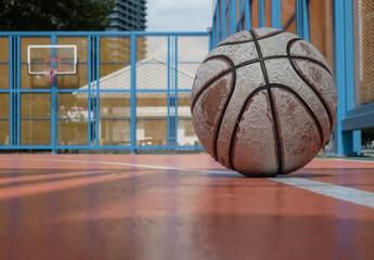 A heavily used basketball rests on an outdoor court, with a hoop and fiberglass backboard visible beneath the industrial Ring Road Bridge in the background. Space for text.