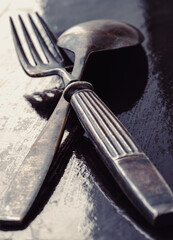 Ancient worn vintage cutlery on the dark background. Crossed black metal spoon and fork in dark tone, Highlighting its texture and design, use it as your Space for text, Design, Wallpaper and Poster, 