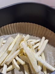 Close-up of frozen French fries spread on parchment paper inside an air fryer basket, ready to be cooked for a quick and crispy homemade snack.