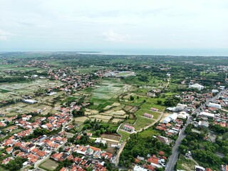 Fototapeta premium Wide aerial view of suburban town with red roof houses blending into green farmland landscape