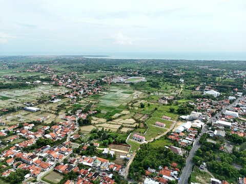 Wide aerial view of suburban town with red roof houses blending into green farmland landscape