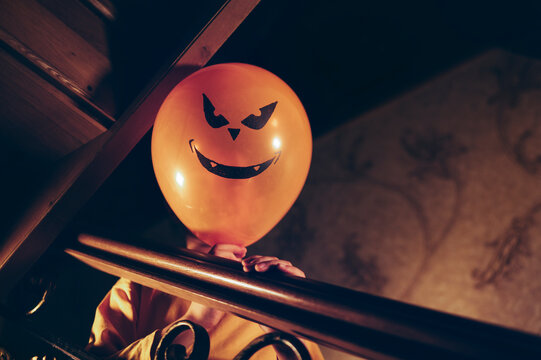 Child with pumpkin face balloon fooling around indoors on Halloween