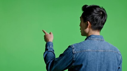 Young Man Pointing Forward While Standing with Back View in Studio Using Green Background for Advertising Presentation and Copy Space Concept