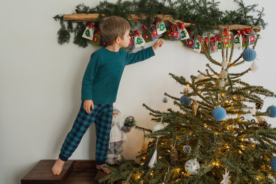 Boy opens felt advent calendar with presents near decorated Christmas tree