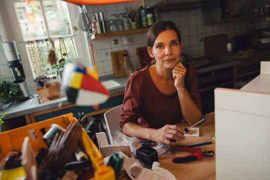 Woman with hand on chin sitting near table at home