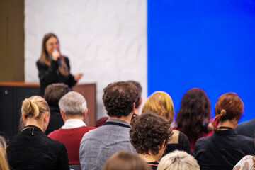 Speaker delivers a presentation to an attentive audience in a conference room. Blue backdrop creates a professional atmosphere for a seminar or workshop.