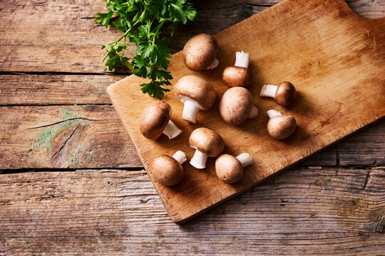 Fresh champignon mushroom group on rustic wooden board with parsley