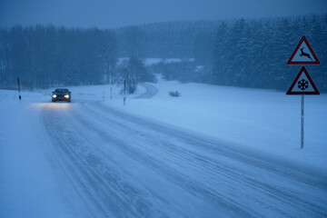 Car driving on snowy road in Moerlbach Bavaria with forest and traffic sign