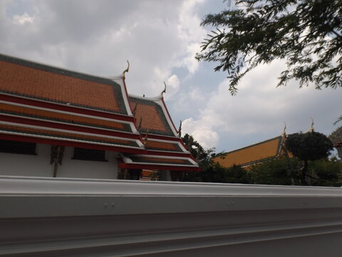 Traditional Thai temple roof with vibrant orange tiles, elegant chofa ornaments, and a serene cloudy sky

