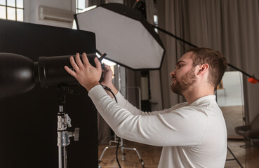 A photographer is adjusting a professional studio light setup, preparing for a photoshoot in a modern studio environment.