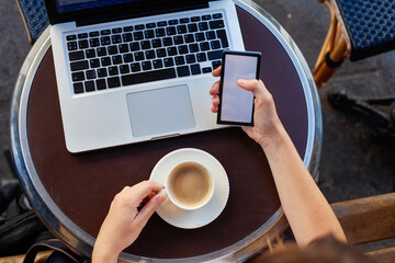 closeup of hands using smartphone with empty blank screen and laptop computer in cafe, hands with mobile phone and coffee