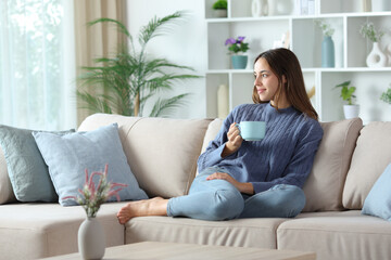 Satisfied woman in blue looking away drinking coffee at home