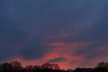 Dramatic dark evening sky with bright red sunset above winter trees
