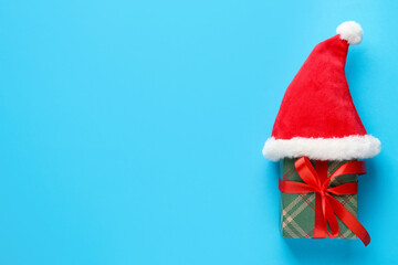 Christmas gift with Santa hat on light blue background, top view. Space for text