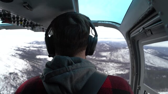 A stationary shot from inside a helicopter cockpit looking over the passenger shoulder as he flies a scenic tour over snow-covered mountains and wilderness near Whitehorse, Yukon