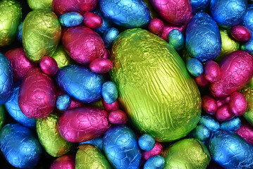 Collection  of colourful foil wrapped chocolate easter eggs in pink, blue, yellow and lime green with a large green egg in the middle.