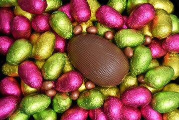 Selection of colourful foil wrapped chocolate easter eggs in pink, red, yellow and lime green with a large brown milk chocolate egg in the middle.