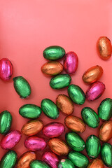 Small colorful pink, green, orange and gold foil wrapped chocolate mini easter eggs, against a peach orange background.