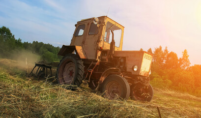 Fototapeta premium Old tractor working in a rural field at sunset