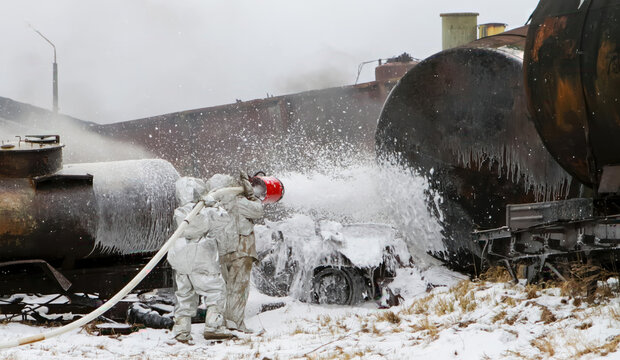 Firefighters spray foam on a large tank after a train derailment in snowy conditions