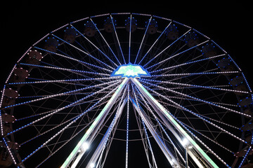 Fototapeta premium Low-angle night photograph of a large illuminated Ferris wheel against a deep black sky.