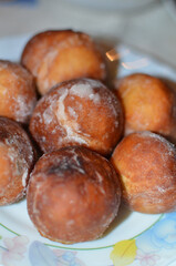 Freshly made homemade doughnuts coated in a generous layer of powdered sugar, piled on a colorful floral plate. 