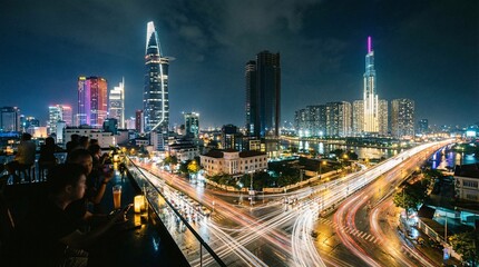 Obraz premium Vibrant cityscape at night with people enjoying drinks on rooftop bar overlooking busy highway and skyscrapers